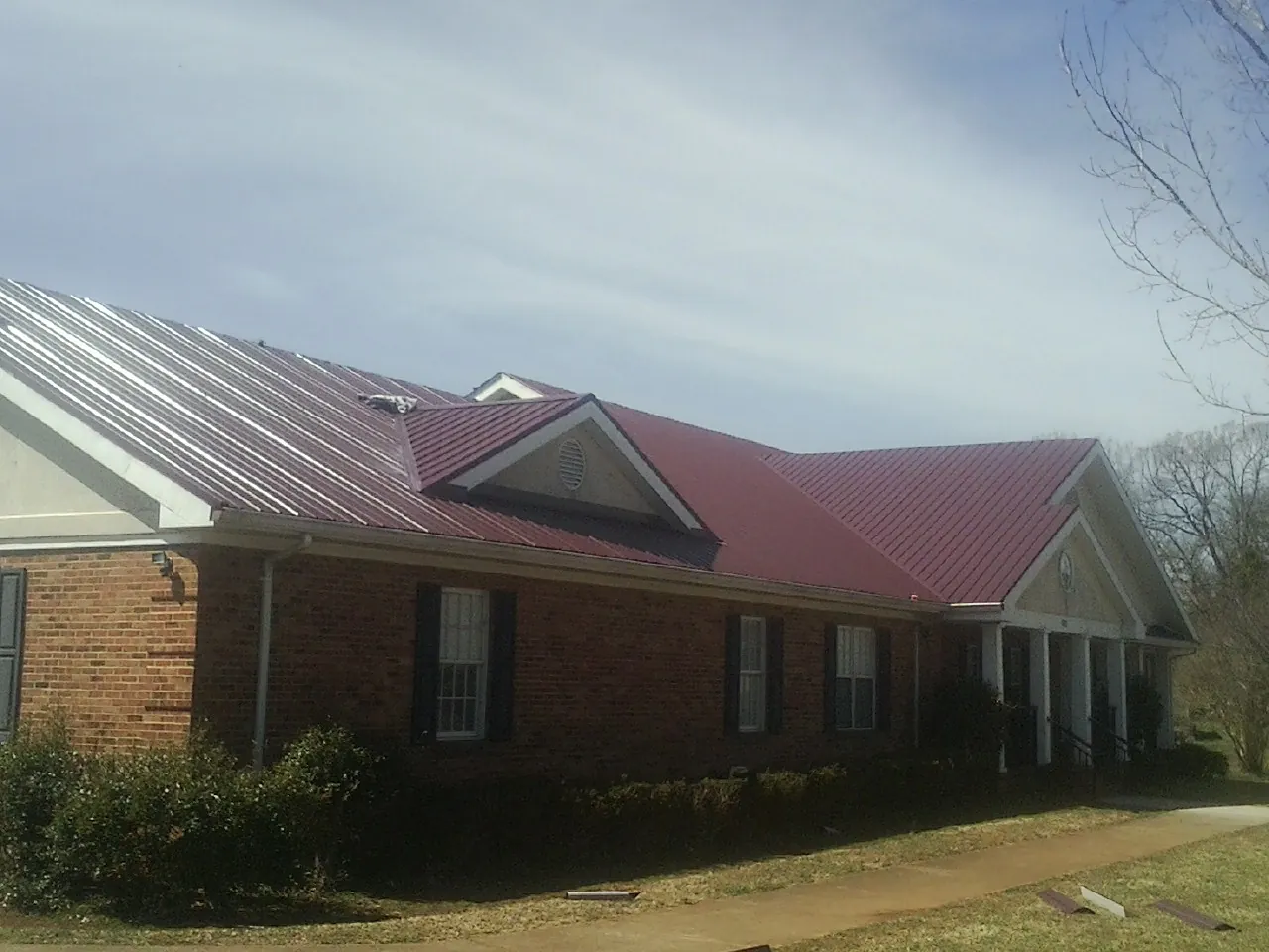 Red metal roof with gabled entries on a long brick building, from a Hail Damage Roof Repair job in Bodega Bay