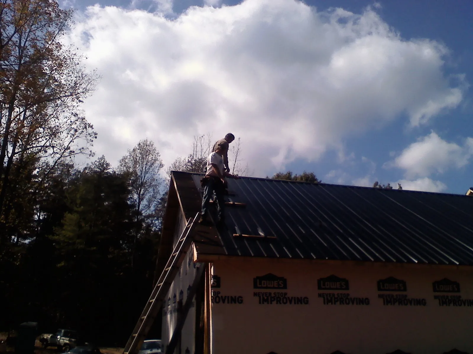 Roofer fastening dark metal panels high against a cloudy sky, from a Roof Inspection job in Bodega Bay