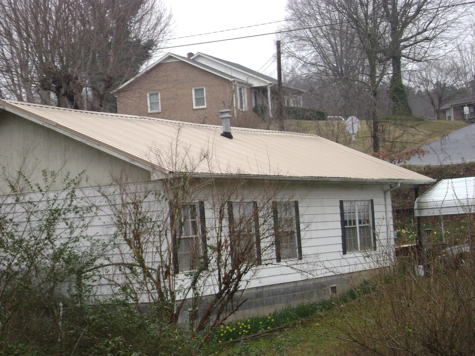 Tan metal roof on a white sided house set into a hillside — Commercial Roofing by Roofing Brothers in Bodega Bay